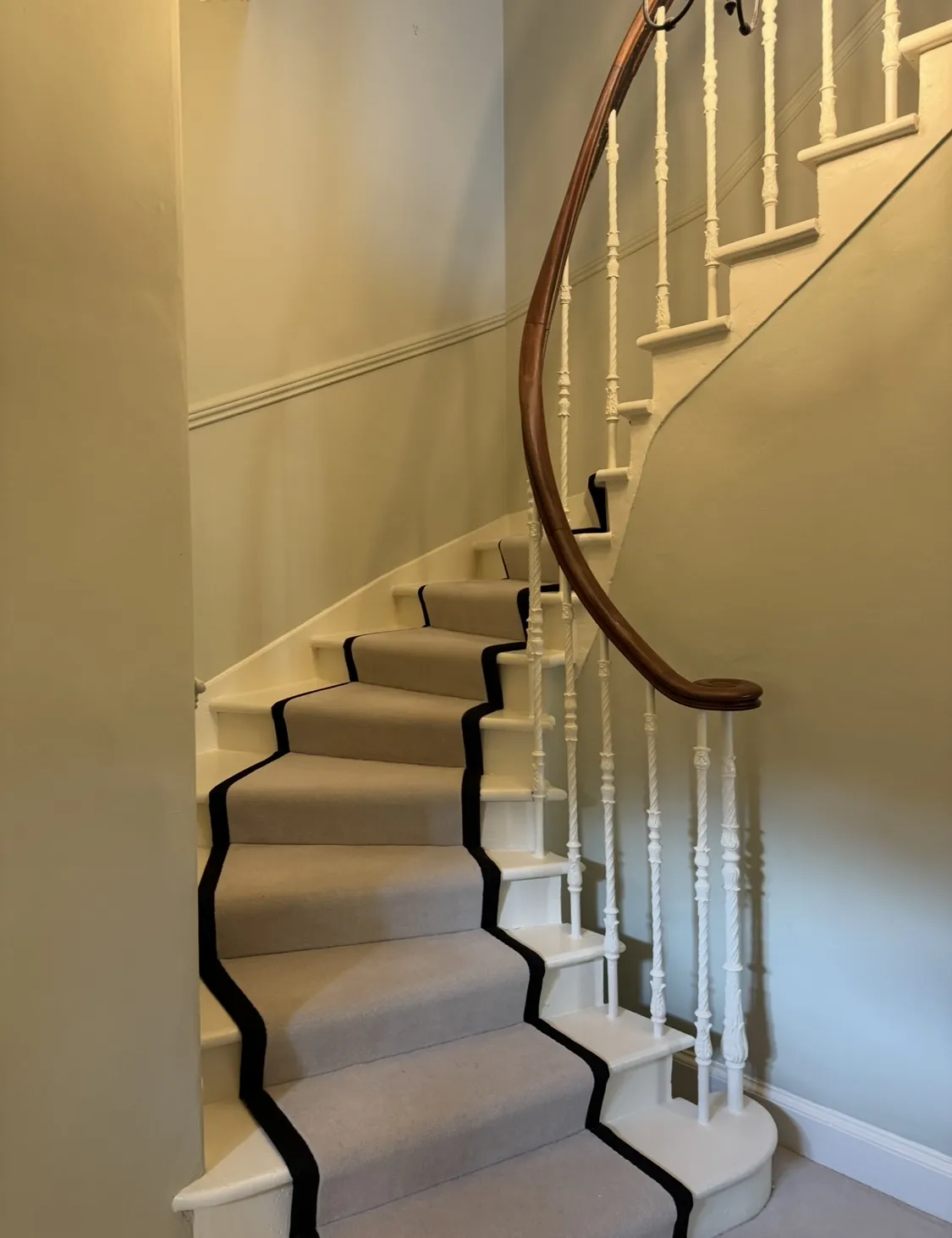Decorated spiral stairs with a rug running down the middle with a classic wooden banister and neutral coloured walls